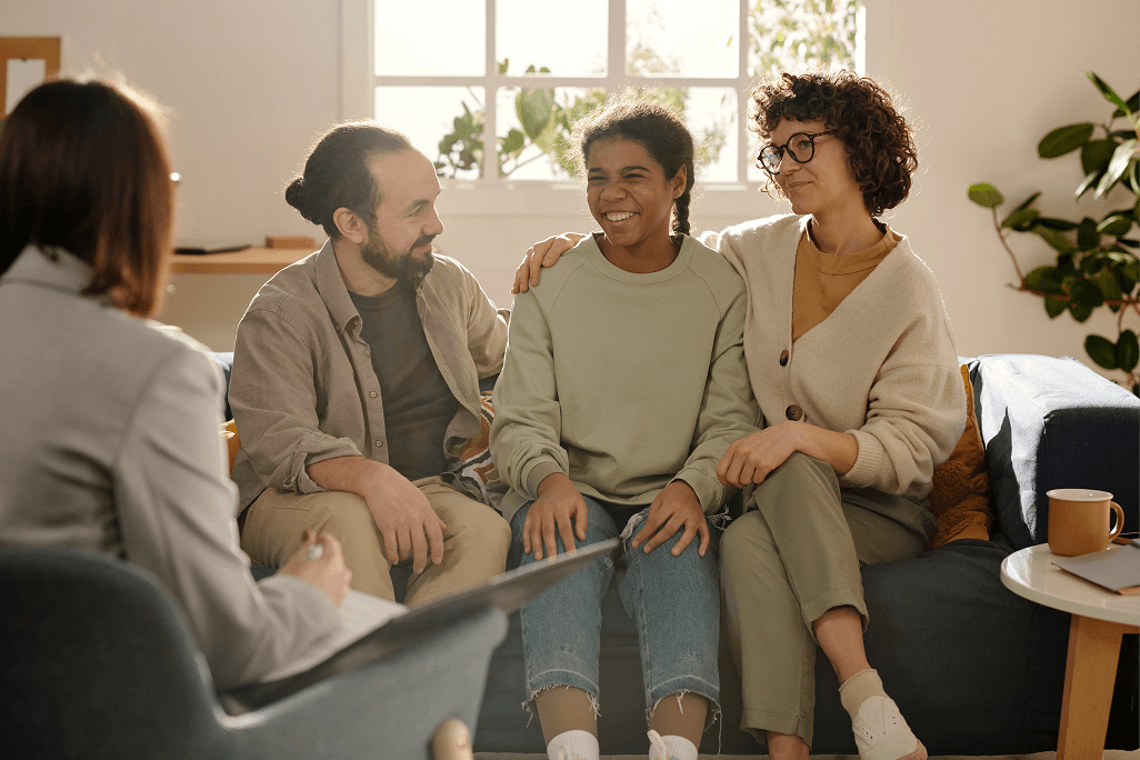 Three people sitting on a couch talking to each other.